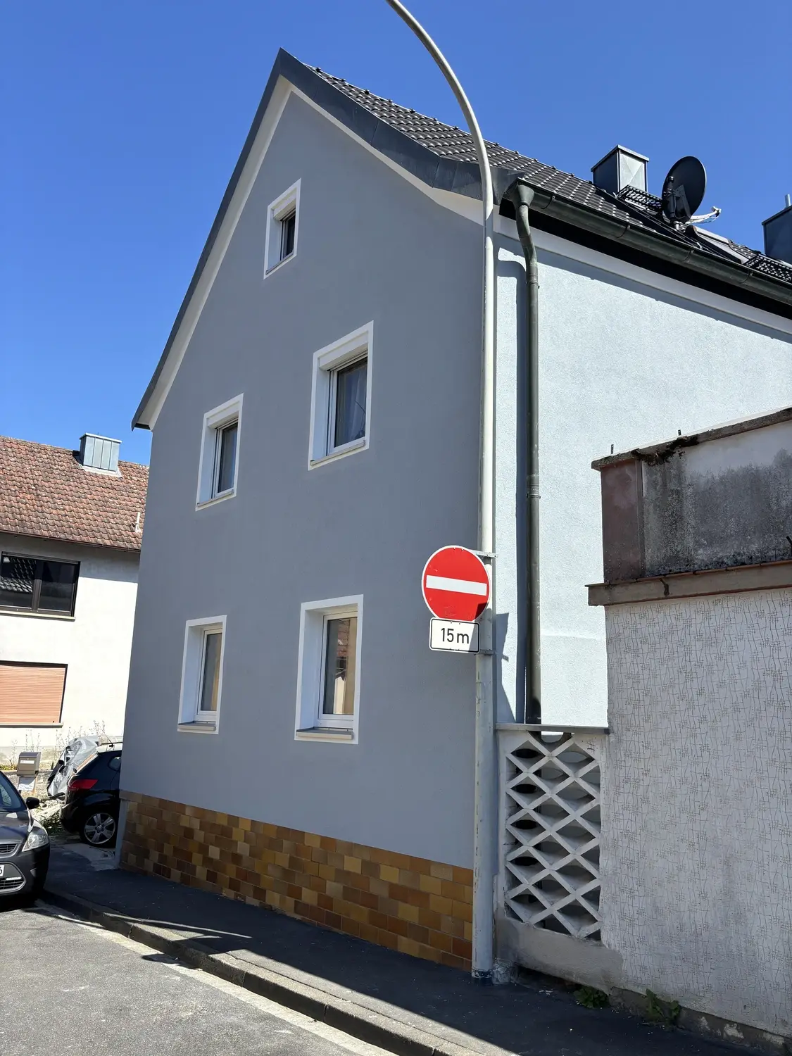 Hellblau gestrichenes Wohnhaus mit braunem Ziegelsockel nach der Sanierung