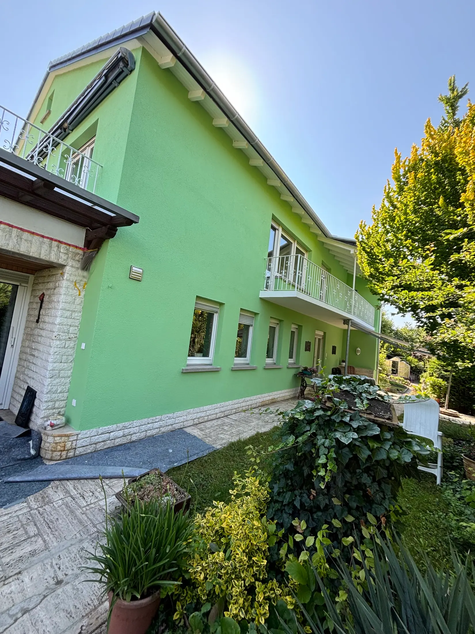 Fertig grün gestrichenes Wohnhaus mit Natursteinsockel und weißen Fenstern in Hanglage