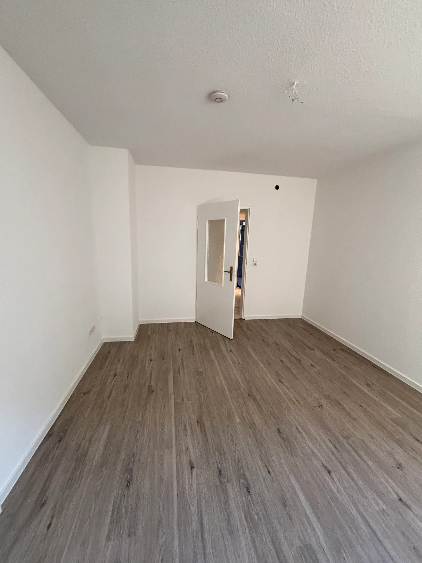 Renoviertes Zimmer mit grauem Vinylboden und geöffneter weißer Zimmertür