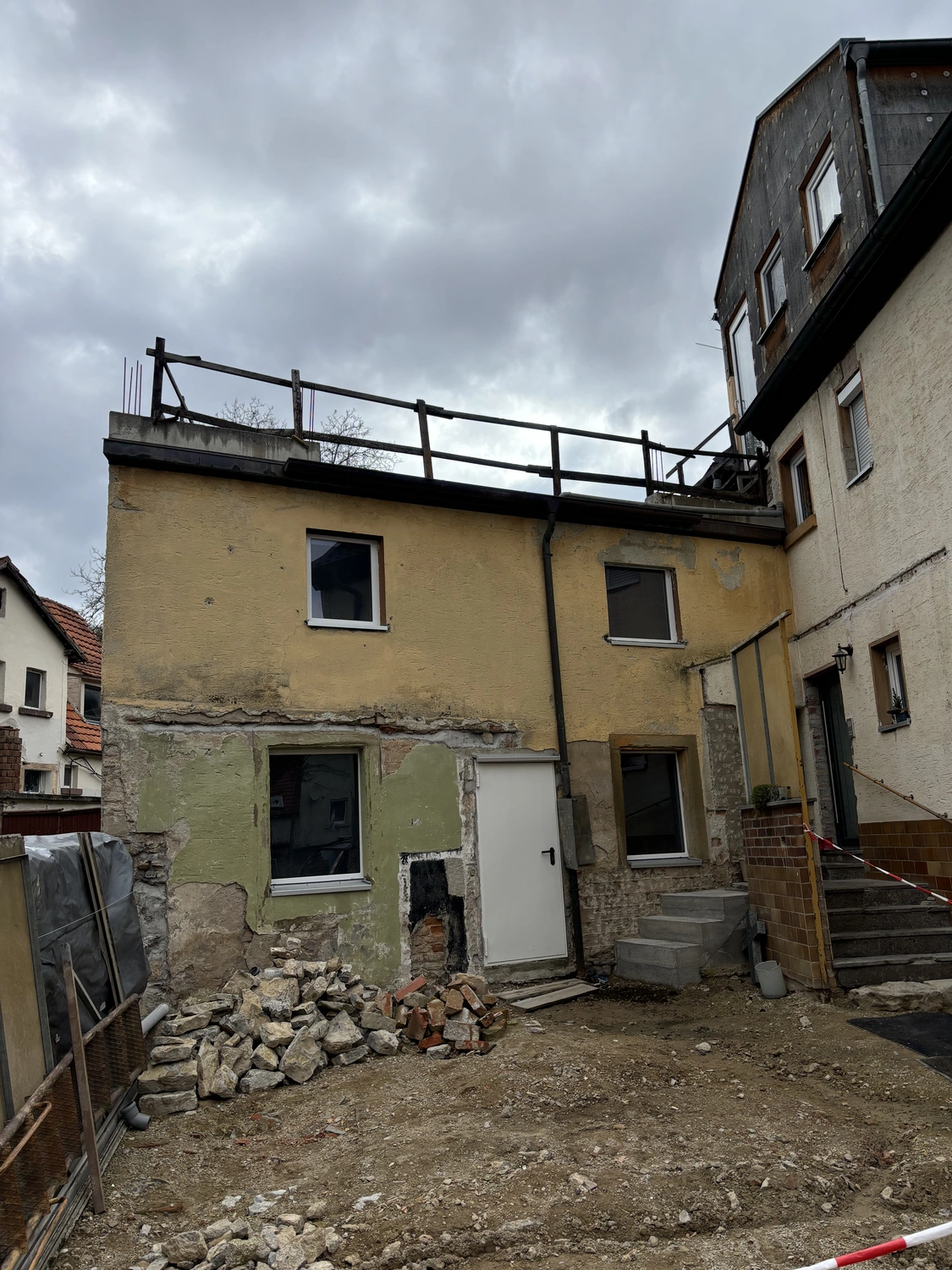 M. Ulusoy & Söhne GbR - Malermeisterbetrieb - Hinterhof eines im Umbau befindlichen Hauses mit freiliegendem Backsteinmauerwerk, Stein- und Ziegelhaufen und bewölktem Himmel