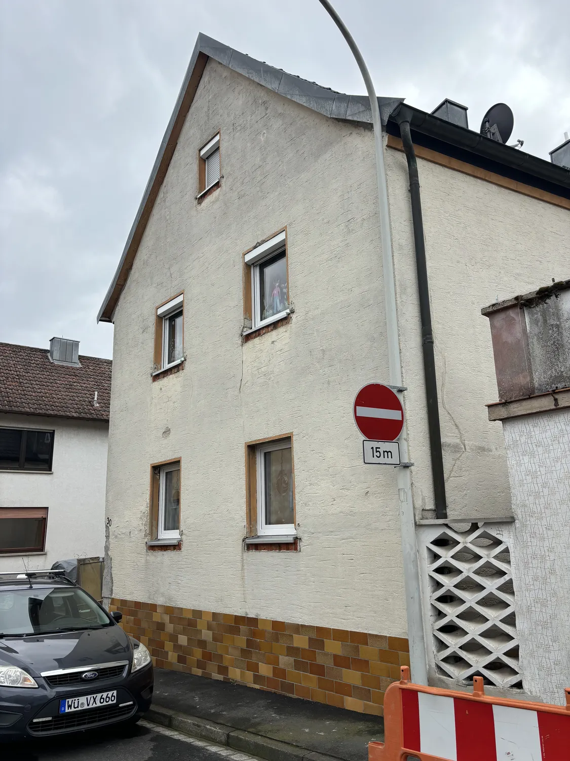 M. Ulusoy & Söhne GbR – Malermeisterbetrieb – Zweistöckiges beiges Haus mit kleinen Fenstern, ein geparktes schwarzes Auto und ein Einfahrtsverbotsschild mit 15-Meter-Abstandsmarkierung davor an einem bewölkten Tag